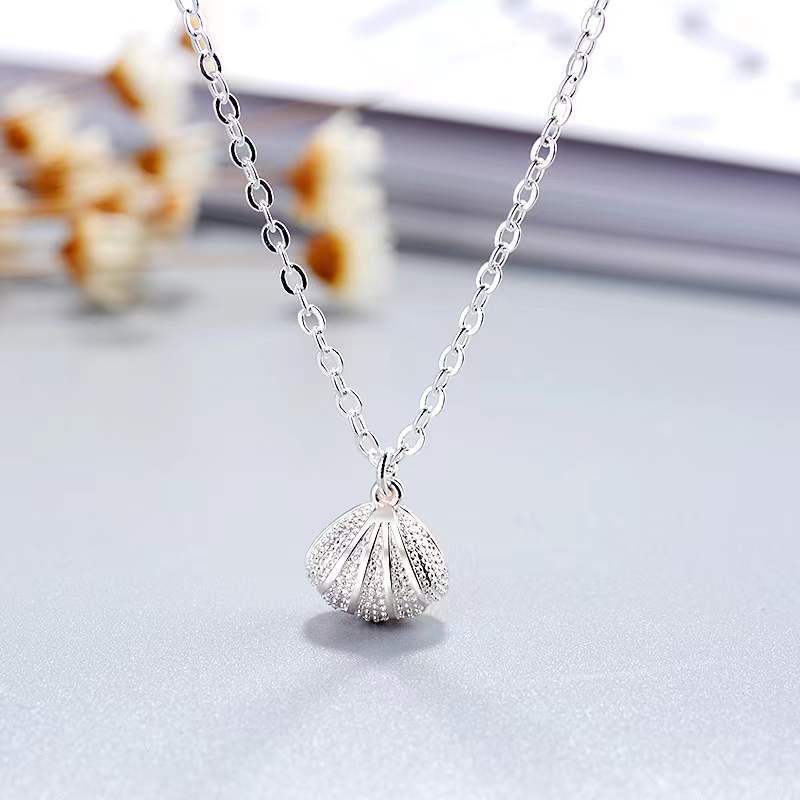 Elegante Halskette aus Sterlingsilber mit Muschelperle und floralen Anhänger auf hellem Hintergrund.