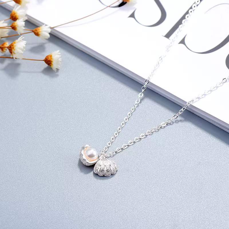 Elegante Halskette aus Sterlingsilber mit Muschelperle und floralen Anhänger auf hellem Hintergrund.