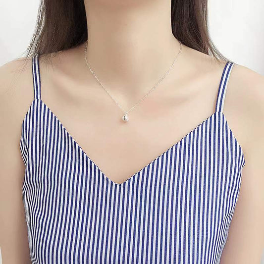 Elegante Halskette aus Sterlingsilber mit Muschelperle, getragen von einer Frau in einem gestreiften Top.