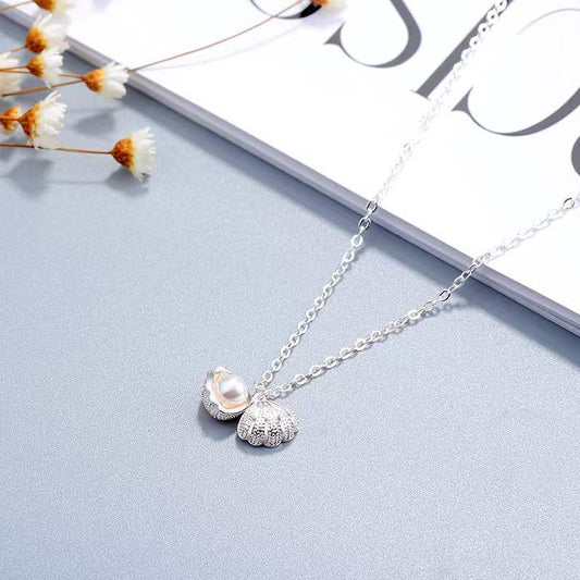 Elegante Halskette aus Sterlingsilber mit Muschelperle und floralen Anhänger auf hellem Hintergrund.
